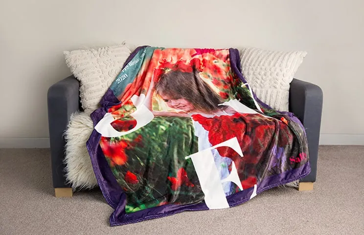 Una coperta di visone personalizzata di Printerpix con un bambino sopra, drappeggiata su un divano. La parola "amore" è visibile.