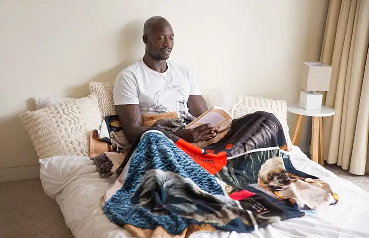 Un uomo legge con una coperta personalizzata di Printerpix con un design a collage di cani sulle sue ginocchia.