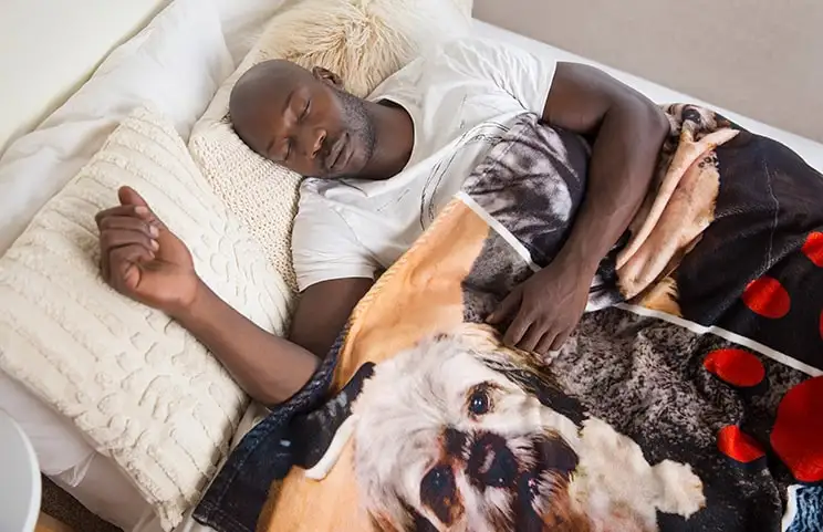 Un uomo dorme sul letto sotto una coperta personalizzata di Printerpix con design di cani.