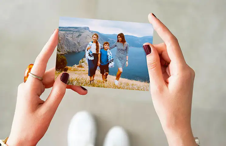 Mani che tengono una stampa fotografica di tre bambini in vacanza